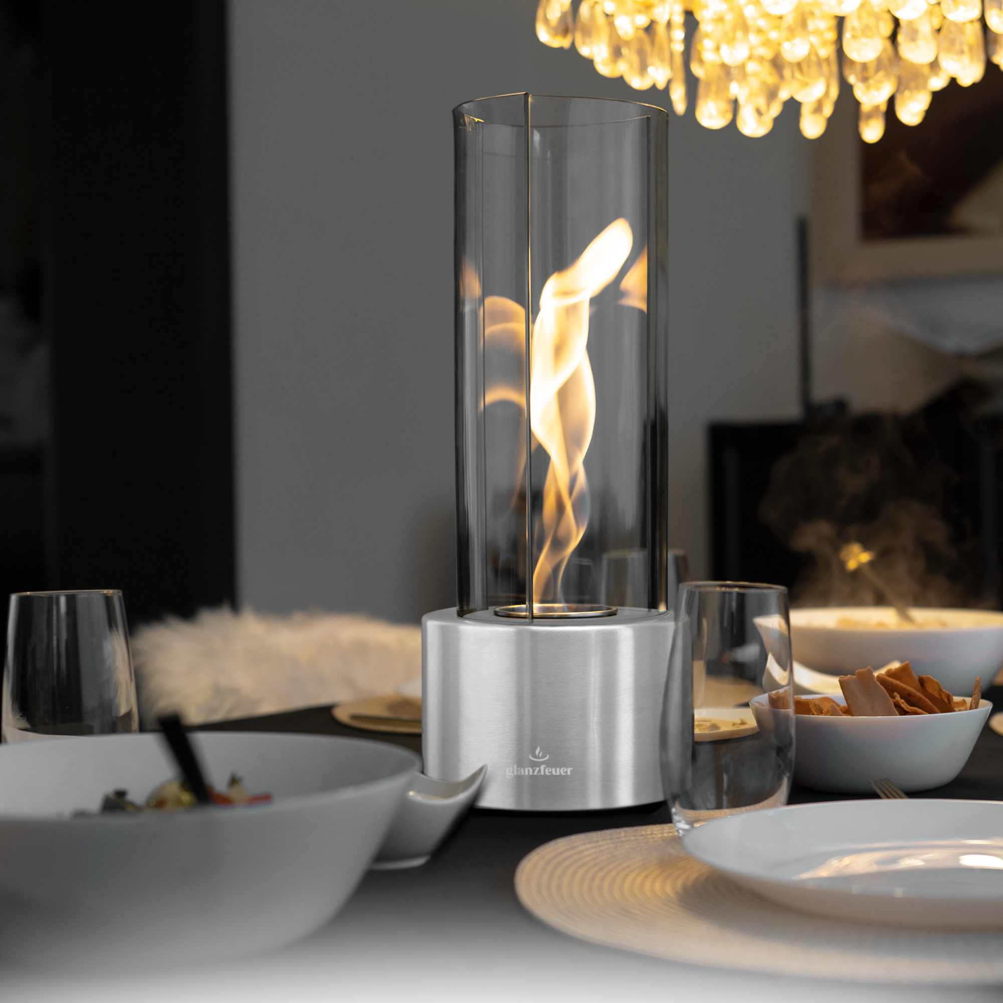 Eleganter Tischkamin mit Glaszylinder und Edelstahlfuß, sorgt für stilvolle Atmosphäre beim Essen oder gemütlichen Abenden.